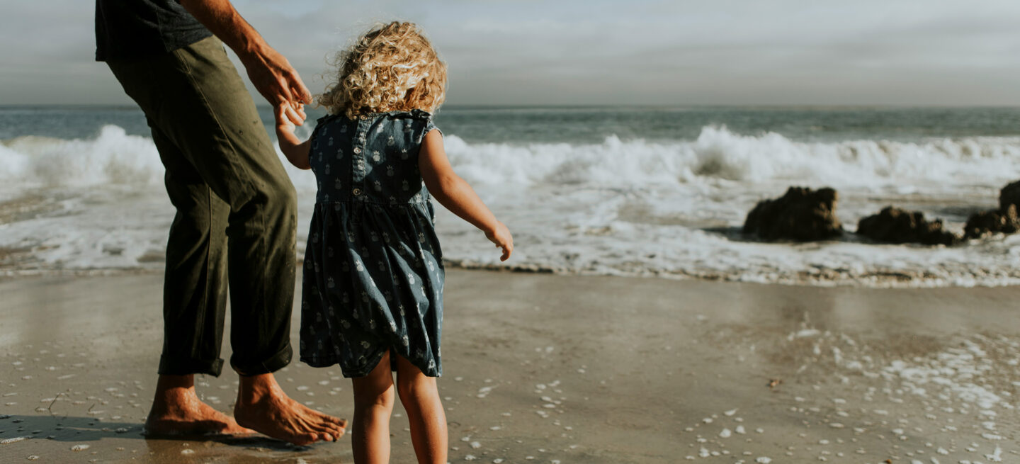 Father holding daughters hand by the ocean