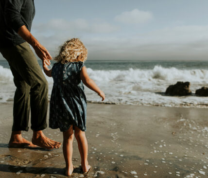 Father holding daughters hand by the ocean